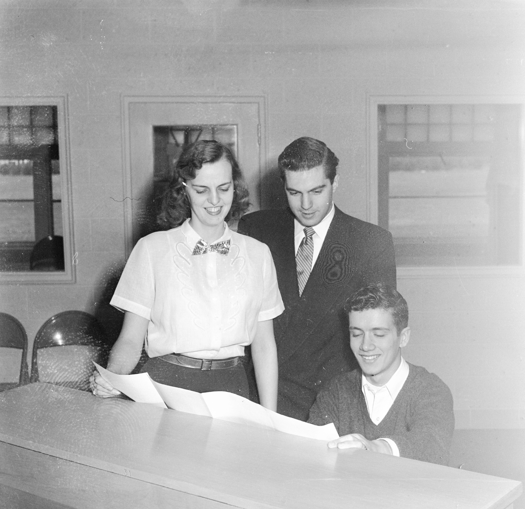Black and white photo of three people looking at piano