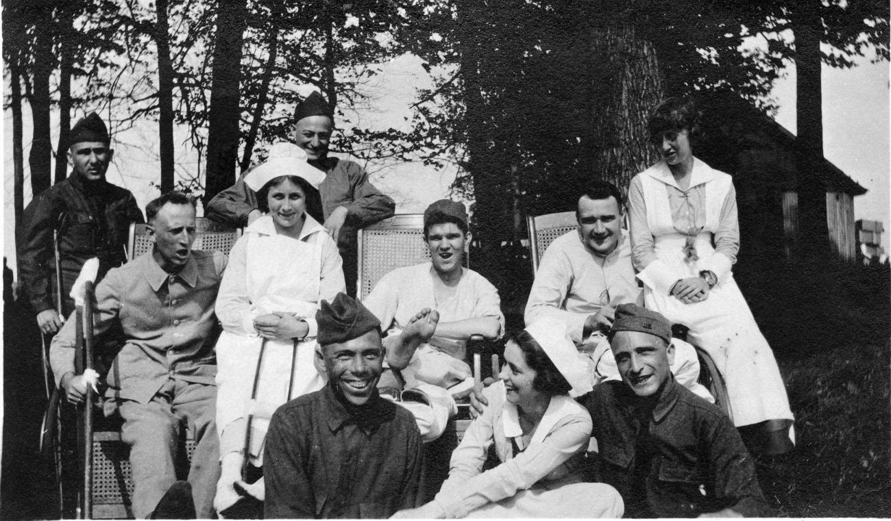 Black and white photo of seven World War I soldiers and three nurses standing and seated on wheelchairs