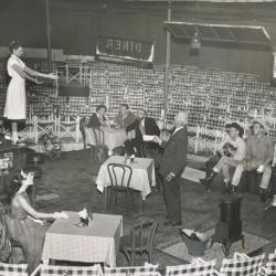 Black and white photo of actors posed on a stage surrounded by empty seats