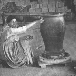 Black and white photo of a woman kneeling on the floor next to two large urns