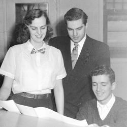 Black and white photo of three people looking at piano