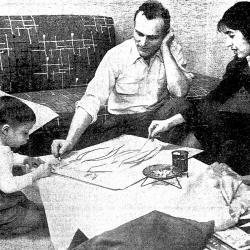 Black and white image of a child and two adults kneeling around and working on a drawing on a low platform
