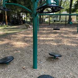 Color photo of green fitness station and swings in background on mulched playground