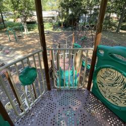 Color photograph looking down over railing at top of climbing gym and slide with mulched park and trees in background
