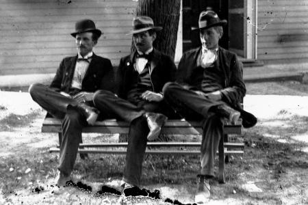 Black and white photo of three men sitting on a bench