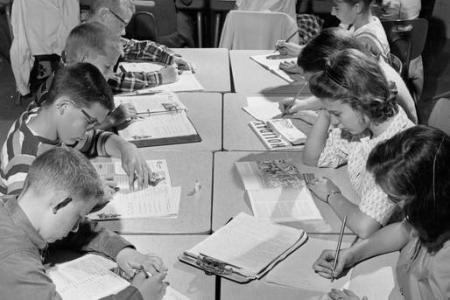 Black and white photo of children at desk cluster with heads bent over open books