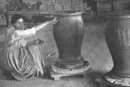 Black and white photo of a woman kneeling on the floor next to two large urns