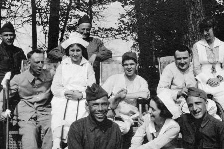 Black and white photo of seven World War I soldiers and three nurses standing and seated on wheelchairs