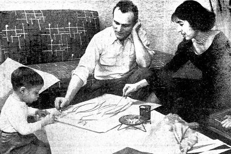 Black and white image of a child and two adults kneeling around and working on a drawing on a low platform
